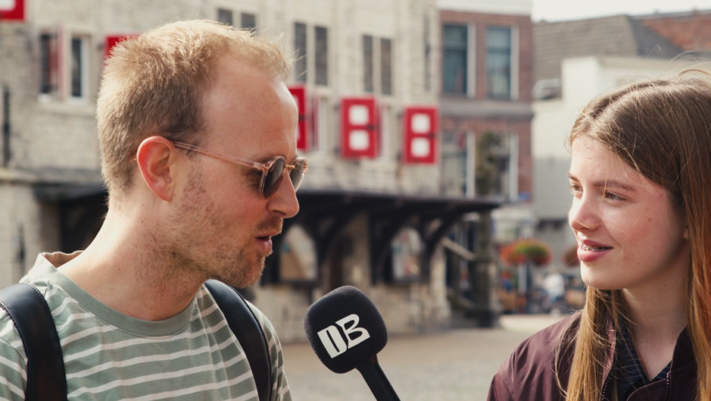 Interviewer Mette met microfoon op straat, interviewt een jongen